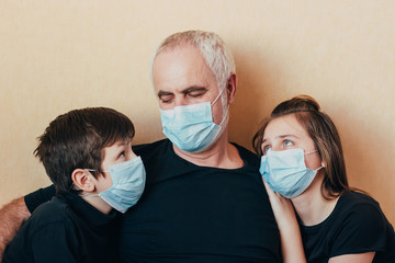 grandfather and grandchildren in face masks sit hugging sadly thinking about restrictions imposed due to coronavirus pandemic. Family support and care during quarantine and world epidemic