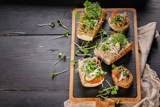Bruschettas and canapes with turkey pate and microgreens on a dark rustic background. Traditional Mediterranean cuisine. Delicious homemade breakfast or snack. Copy space