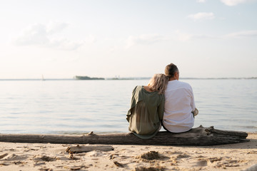 man and woman are sitting on a log by the sea and looking into the distance