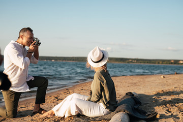 a man on the beach photographs on camera a woman who sits on a plaid in the sand