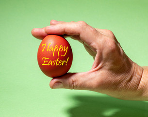 Creative easter square photo. Female hand gently holding one traditional colored red Easter egg with inscription Happy Easter. Holiday concept.