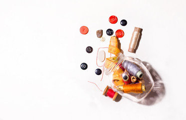 Glass jar with threads and buttons on a white background top view. Copy space. The concept of repairing things and sewing.