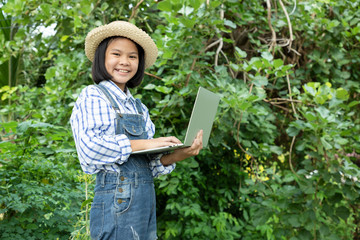 Young girl using a notebook computer in the front garden with a bright smile. She has ideas for nature conservation and research on tree and plant species. Concept of environmental conservationists.