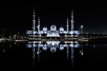 Fototapeta na wymiar Iconic Islamic Site: Grand Mosque in Abu Dhabi, United Arab Emirates at night with a reflection in the pool showing off its beautiful colours of purple in the sky and water.