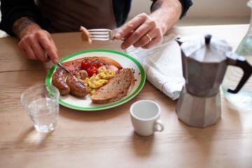 A man eats a traditional cooked breakfast at a wooden table