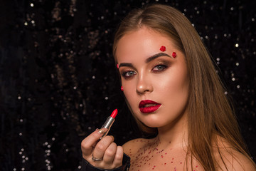 The girl who paints her lips with lipstick. Woman portrait on a black shiny background.