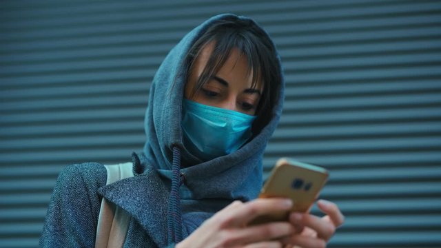 closeup Woman in hood and protective face mask Using Smartphone outdoors 4K. female reading news on cell phone, using app, communicating in social media. Cold spring or autumn.