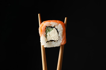 Chopsticks with sushi roll on black background, close up. Japanese food © Atlas