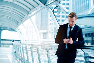 Handsome business man wearing a black suit and using smartphone to chat with business partners in...