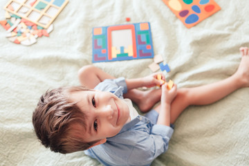 Obraz na płótnie Canvas The happy boy sits on the bed and lays puzzles