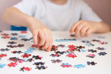 The child collects a puzzle. Elements of the puzzle are laid out on a white table. Children's hands during the game. Home leisure.