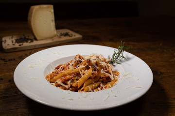 Penne all'Amatriciana with grated Pecorino Romano and garnish rosemary from the wooden table of an old tavern