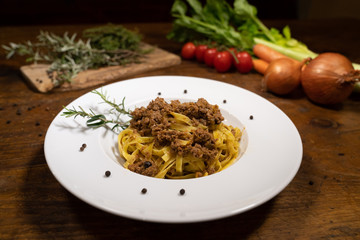 egg pasta tagliatelle with wild boar sauce with juniper berries and rosemary on a wooden table in an old tavern