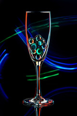 glass balls in a wine glass on a black background with colored light rays
