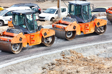 Large and heavy orange vibratory rollers compact the hot asphalt on the new road.