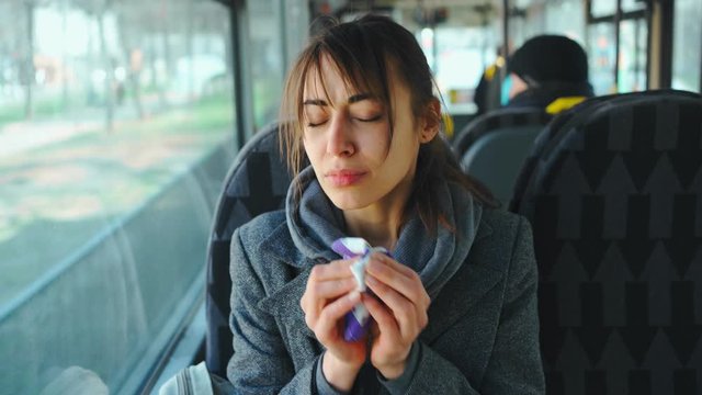 young woman sneezes and Coughing while sitting in city bus and puts on protective mask. sick female in public transport. prevention spread of coronavirus and viral infection in public places.
