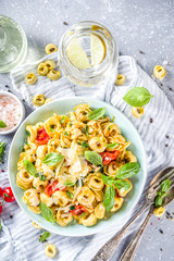 Italian ravioli, tortellini pasta with parmesan cheese and vegetables - spinach, tomatoes, mushrooms and basil, On grey stone background copy space