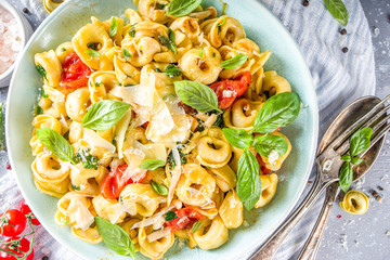 Italian ravioli, tortellini pasta with parmesan cheese and vegetables - spinach, tomatoes, mushrooms and basil, On grey stone background copy space