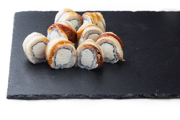 .maki sushi with eel and soft cheese on a stone board. on a white background