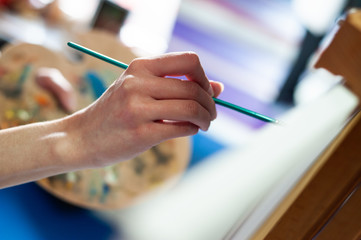 Closeup of brush and palette.Girl holding paintbrush in home art studio.
