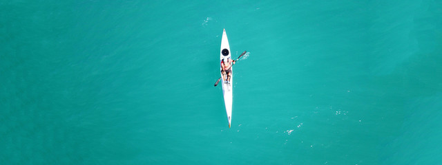 Aerial drone ultra wide top down photo of man paddling in sport canoe in emerald calm water lake