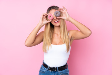 Young Uruguayan woman over isolated pink background holding donuts in eyes