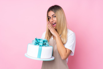 Young Uruguayan pastry woman with a big cake over isolated pink background whispering something