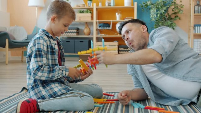 Joyful family dad and son are having fun with wooden toys relaxing laughing at home enjoying game. Modern lifestyle, people and entertainment concept.