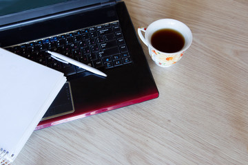 A cup of tea next to a laptop and a bolknot