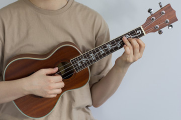Fototapeta na wymiar Woman hands playing ukulele on the gray background