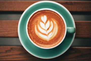 Cup of cappuccino with latte art on wooden background. Flat lay style.