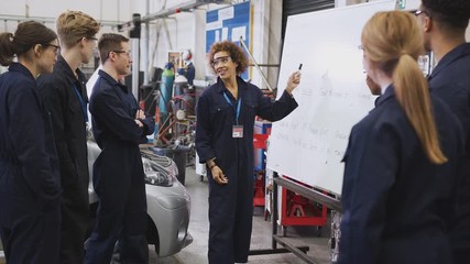 Female tutor by whiteboard with students teaching auto mechanic apprenticeship at college - shot in slow motion