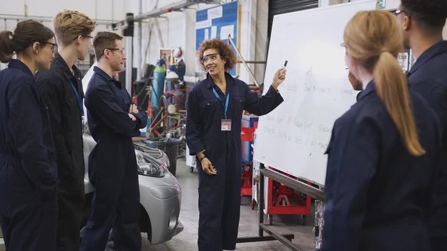Female tutor by whiteboard with students teaching auto mechanic apprenticeship at college - shot in slow motion