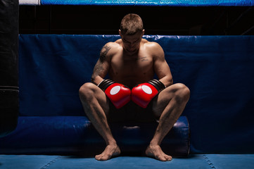 Boxer sits in gloves near the ring with his head bowed. The concept of sports, boxing, mixed...