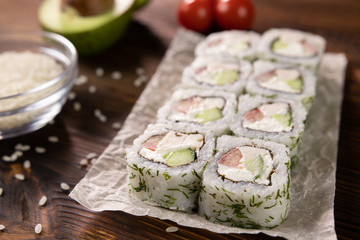 rolls with avocado, tomato, chicken and cheese on paper on a dark wooden board