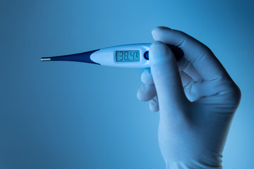 Hand in a medical glove holds a thermometer. Ambient blue light.
