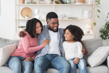 Loving Black Man Embracing Wife And Daughter On Couch At Home