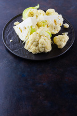 Cauliflower on a black plate. Sliced fresh cauliflower on a dark background. Slices of organic cabbage on a plate. Top view. Copy space