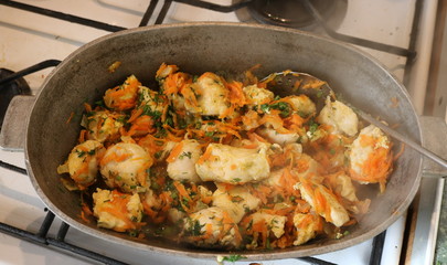Chunks of white meat with carrots and herbs in a cast-iron pot on the stove. Photographed in room light through steam coming from a pot. 