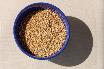 Green buckwheat in blue porcelain bowl, natural shadow.Dry unroasted whole grain superfood flat lay.Organic healthy food, weight loss, reduce inflammation,help manage diabetes,maintaining heart health