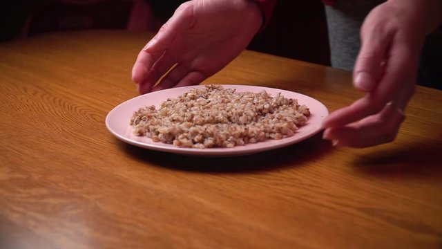 buckwheat on a pink plate is served on the table; cooking at home on a brown wooden table