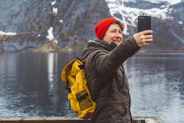 Traveler man taking self-portrait with a smartphone against the background of snowy mountains,...