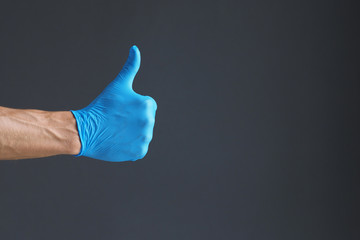 Hand wearing blue latex glove with thumb up gesture on dark background. Copy space.
