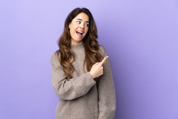 Obraz premium Woman over isolated purple background surprised and pointing side