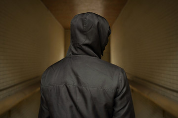 A man in a hood on the street. Social problems, drug addiction and criminal activity. The view from the back.
