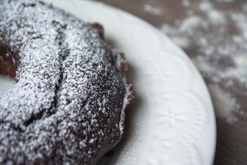 Chocolate cake with a hole in the centre and sugar powder sprinkled on top, on the background are a teapot and teacup with tea