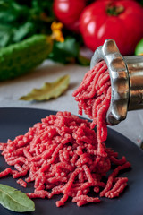 Fresh red meat mincing with old metal manual grinder, viewed in close-up on grey stone background .