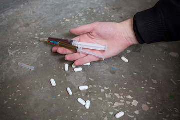 Addict hand with syringe and pills on the floor. International Drug Abuse Day. Addiction concept.