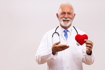 Portrait of senior doctor with stethoscope showing heart shape on gray background.