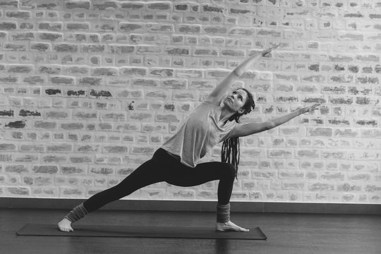 woman with dreadloks doing stratch on yoga mat against brick wall black and white photography